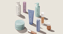 Fenty Hair collection, Fenty Skin Hydra Vizor SPF moisturizer, Fenty Beauty foundations, and Fenty Beauty Gloss Bomb Universal Lip Luminizer products standing up on a cream background.