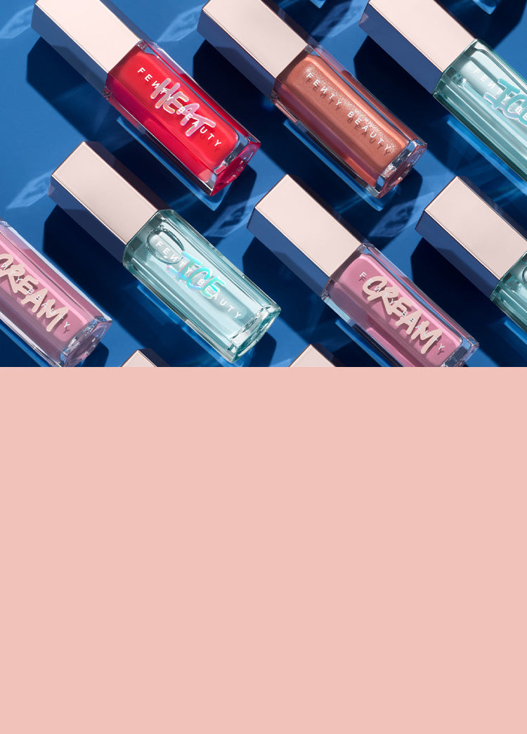 Editorial shot of Gloss Bomb Universal Lip Luminizer in Fenty Glow, Gloss Bomb Heat in Hot Cherry, and Gloss Bomb Ice in Cold Hearted lined up against a blue background.